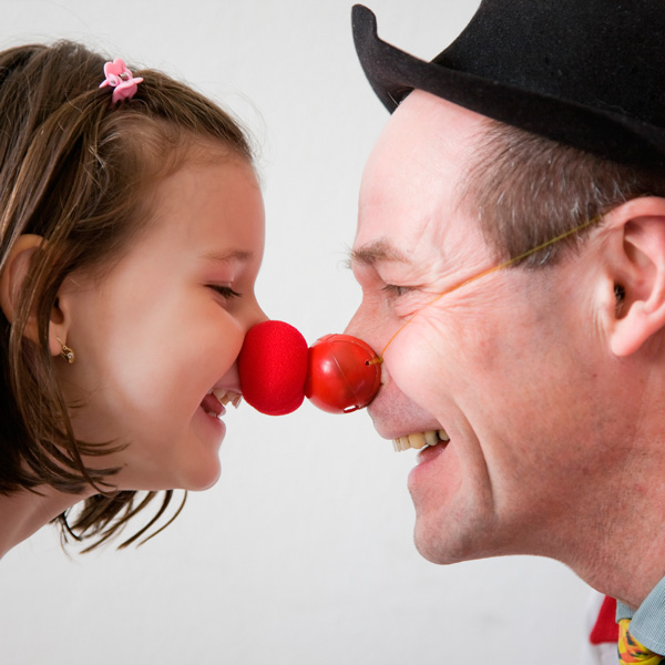 Kind und Clown, die sich mit ihren roten Clownnasen berühren.